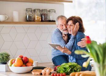 Ein Porträt eines glücklichen, verliebten älteren Paares zu Hause, das mit einem Tablet nach einem Rezept sucht. - HPIF21447
