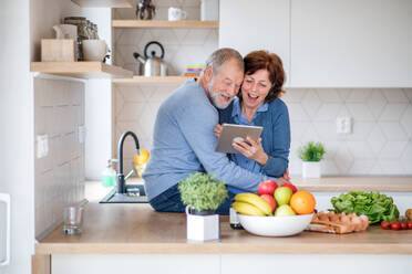 Ein Porträt eines glücklichen, verliebten älteren Paares zu Hause, das mit einem Tablet nach einem Rezept sucht. - HPIF21448
