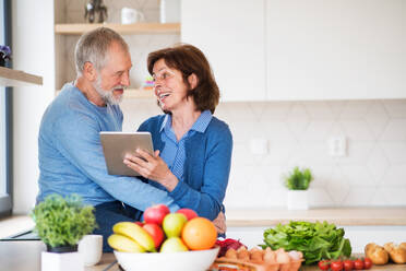 Ein Porträt eines glücklichen, verliebten älteren Paares zu Hause, das mit einem Tablet nach einem Rezept sucht. - HPIF21449