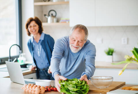 A portrait of happy senior couple with laptop indoors at home, cooking. - HPIF21450