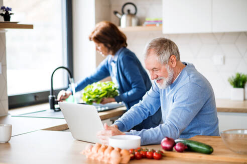 A portrait of happy senior couple with laptop indoors at home, cooking. - HPIF21451