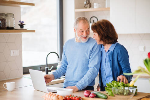 A portrait of happy senior couple with laptop indoors at home, cooking. - HPIF21455
