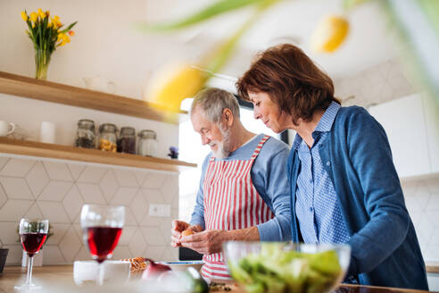 A portrait of happy senior couple in love indoors at home, cooking. - HPIF21459