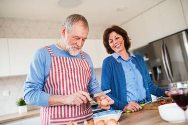 A portrait of happy senior couple in love indoors at home, cooking. - HPIF21460