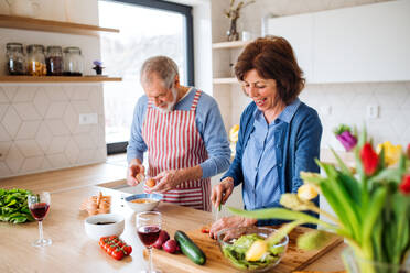 A portrait of happy senior couple in love indoors at home, cooking. - HPIF21461