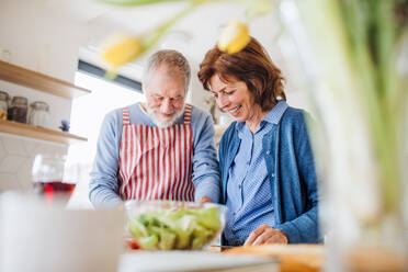 A portrait of happy senior couple in love indoors at home, cooking. - HPIF21464