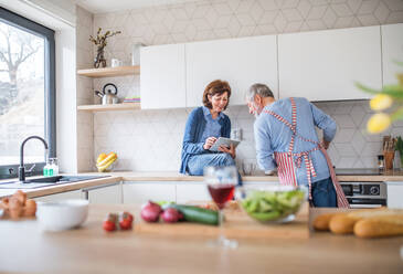 A portrait of happy senior couple in love indoors at home, looking for recipe using tablet. - HPIF21467