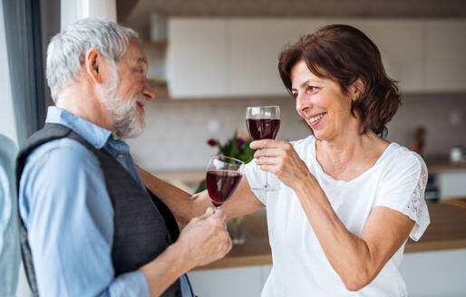 Ein Porträt eines glücklichen, verliebten älteren Paares, das zu Hause mit Gläsern anstößt. - HPIF21477