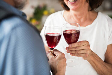 A midsection of senior couple in love indoors at home, clinking glasses with red wine. - HPIF21480