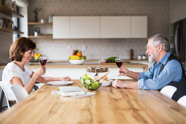 A senior couple in love having lunch indoors at home, talking. - HPIF21483