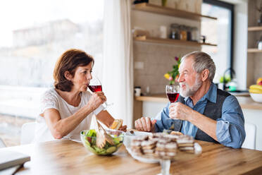 Ein älteres Ehepaar mit Wein, das zu Hause zu Mittag isst und sich unterhält. - HPIF21488