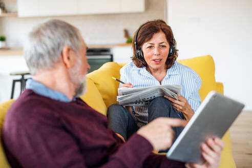 Älteres Ehepaar mit Tablet und Kopfhörern sitzt zu Hause auf dem Sofa und entspannt sich. - HPIF21492