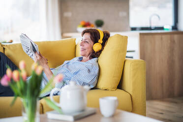 A senior woman with headphones and crosswords sitting on sofa indoors at home, resting. - HPIF21494