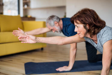 Ein glückliches Seniorenpaar, das zu Hause auf dem Fußboden Übungen macht. - HPIF21515