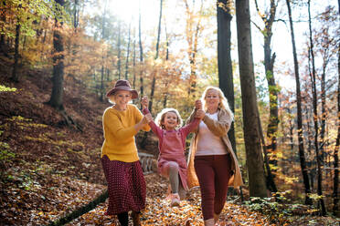 Small girl with mother and grandmother on a walk in autumn forest, having fun. - HPIF21629