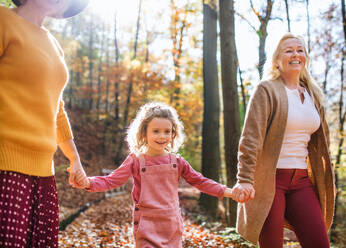 Small girl with unrecognizable mother and grandmother on a walk in autumn forest. - HPIF21630