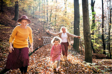 Kleines Mädchen mit Mutter und Großmutter auf einem Spaziergang im herbstlichen Wald, die Spaß haben. - HPIF21631