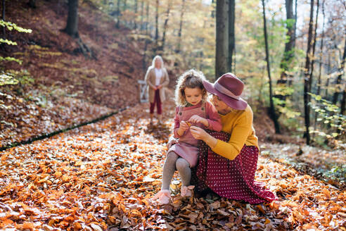 Kleines Mädchen mit Mutter und Großmutter bei einem Spaziergang im Herbstwald, im Gespräch. - HPIF21634