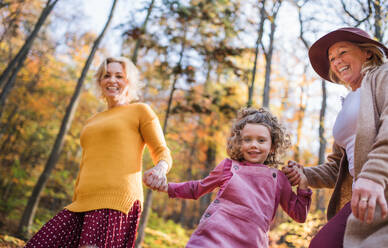 Small girl with mother and grandmother on a walk in autumn forest, having fun. - HPIF21638