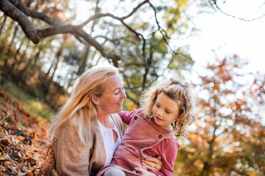 Portrait of small girl with grandmother on a walk in autumn forest, having fun. - HPIF21642