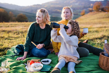 Glückliches kleines Mädchen mit Mutter und Großmutter beim Picknick in der Natur, mit Fernglas. - HPIF21657