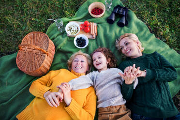 Draufsicht auf ein kleines Mädchen mit Mutter und Großmutter beim Picknick in der Natur, lachend. - HPIF21664