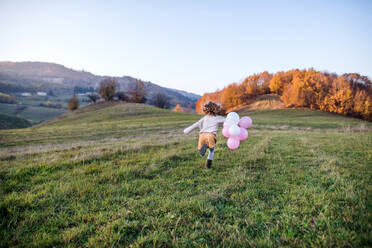 Rear view of cheerful small girl with balloons running in autumn nature. - HPIF21666