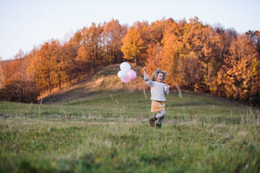 Cheerful small girl with balloons running on meadow in autumn nature. - HPIF21667