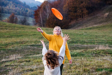Small girl with grandmother on a walk in autumn nature, playing with flying disc. - HPIF21670