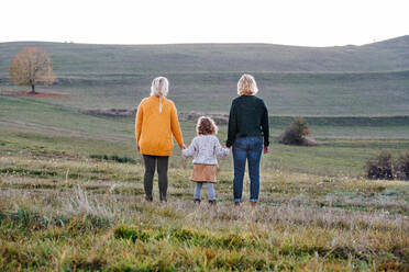 Rear view of small girl with mother and grandmother on a walk in autumn nature, holding hands. - HPIF21673