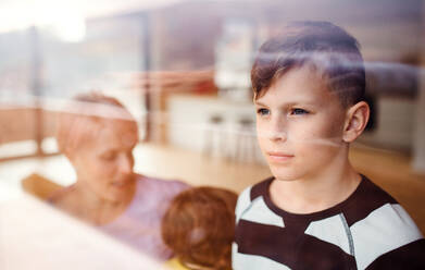 Porträt eines kleinen Jungen mit seiner Familie zu Hause, der aus dem Fenster schaut, aufgenommen durch Glas. - HPIF21687