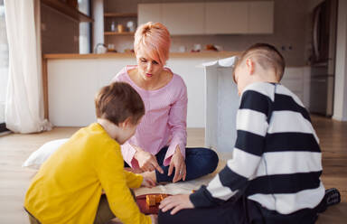 Eine junge Mutter mit zwei Kindern spielt Brettspiele auf dem Boden. - HPIF21689