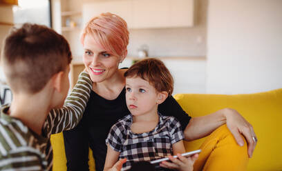 Eine junge Frau mit zwei Kindern sitzt zu Hause auf dem Sofa und benutzt ein Tablet. - HPIF21705