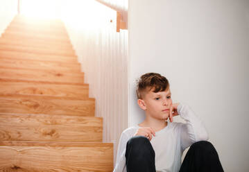 A sad small boy sitting on the floor by the stairs. Copy space. - HPIF21716