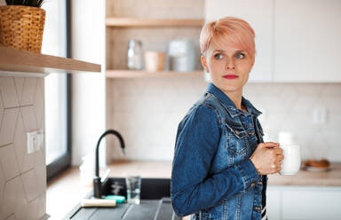 A young attractive woman with a coffee leaning on a counter in a kitchen at home. - HPIF21727