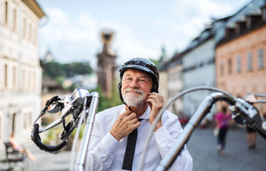 Ein fröhlicher älterer Geschäftsmann mit Motorrad in der Stadt, der seinen Helm aufsetzt. - HPIF21751