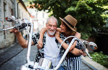 A front view of cheerful senior couple travellers with motorbike in town. - HPIF21760