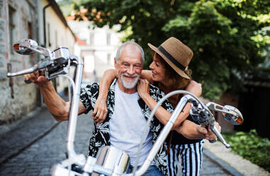 Frontansicht eines fröhlichen älteren Ehepaars, das mit dem Motorrad durch die Stadt reist. - HPIF21760