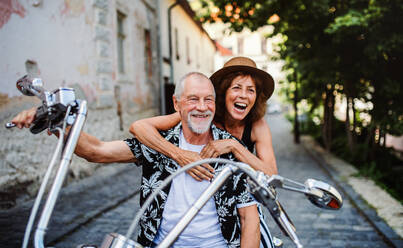 A front view of cheerful senior couple travellers with motorbike in town. - HPIF21762