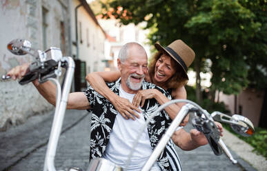 Frontansicht eines fröhlichen älteren Ehepaars, das mit dem Motorrad durch die Stadt reist. - HPIF21763