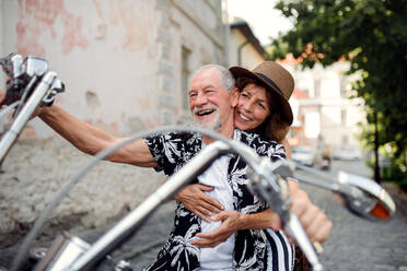 A front view of cheerful senior couple travellers with motorbike in town. - HPIF21765