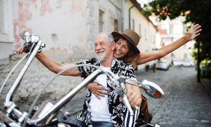 A front view of cheerful senior couple travellers with motorbike in town. - HPIF21766