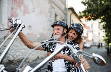Frontansicht eines fröhlichen älteren Ehepaars, das mit dem Motorrad durch die Stadt reist. - HPIF21767