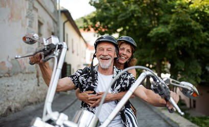A front view of cheerful senior couple travellers with motorbike in town. - HPIF21768