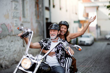 Frontansicht eines fröhlichen älteren Ehepaars, das mit dem Motorrad durch die Stadt reist. - HPIF21769