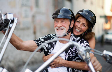 Frontansicht eines fröhlichen älteren Ehepaars, das mit dem Motorrad durch die Stadt reist. - HPIF21771