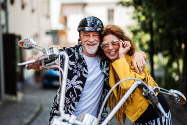 Frontansicht eines fröhlichen älteren Ehepaars, das mit dem Motorrad durch die Stadt reist. - HPIF21776