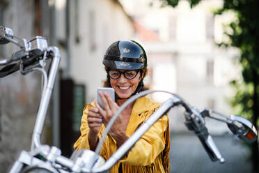 A joyful elderly female tourist poses for a selfie with her motorcycle in the city - HPIF21792