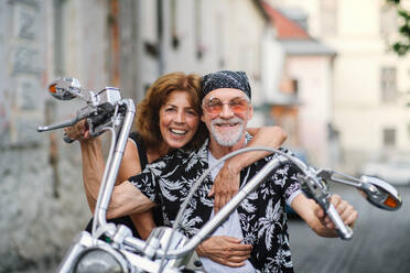 A front view of cheerful senior couple travellers with motorbike in town. - HPIF21807