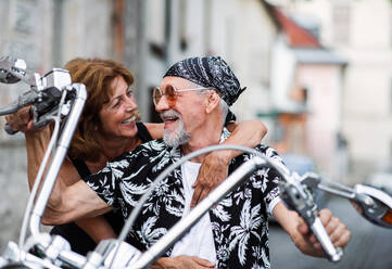 Frontansicht eines fröhlichen älteren Ehepaars, das mit dem Motorrad durch die Stadt reist. - HPIF21808